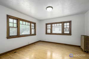 Empty room with light hardwood / wood-style flooring and radiator heating unit