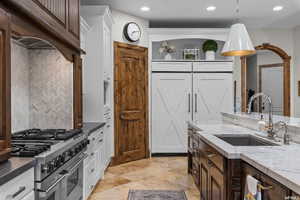 Kitchen featuring decorative light fixtures, range with two ovens, tasteful backsplash, white cabinetry, and sink