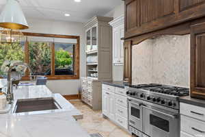 Kitchen with light stone counters, light tile flooring, white cabinetry, double oven range, and sink