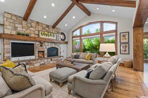 Living room featuring a stone fireplace, high vaulted ceiling, beamed ceiling, and light wood-type flooring