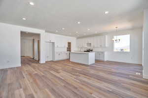 Kitchen with light wood-type flooring, a kitchen island with sink, white cabinets, pendant lighting, and stainless steel range