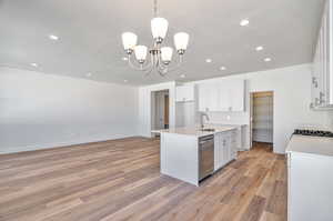 Kitchen with white cabinetry, light hardwood / wood-style floors, an inviting chandelier, a kitchen island with sink, and dishwasher