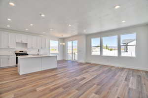 Kitchen with light hardwood / wood-style flooring, stainless steel range, an island with sink, sink, and white cabinetry