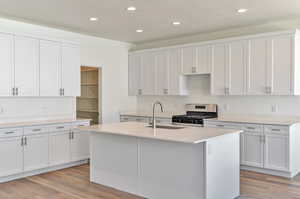 Kitchen featuring light hardwood / wood-style flooring, a kitchen island with sink, gas stove, white cabinets, and sink