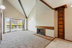 Unfurnished living room with high vaulted ceiling, a brick fireplace, and light tile flooring