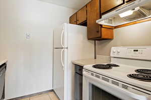 Kitchen with dishwashing machine, stove, and light tile floors