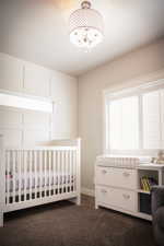 Bedroom with a chandelier, a nursery area, and dark carpet