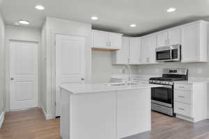 Kitchen with light hardwood / wood-style floors, white cabinetry, a center island with sink, appliances with stainless steel finishes, and sink