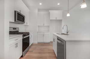 Kitchen featuring white cabinetry, light wood-type flooring, appliances with stainless steel finishes, sink, and pendant lighting