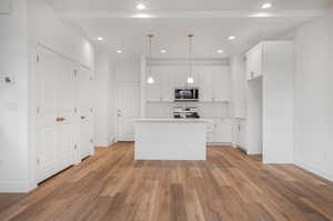 Kitchen with a center island with sink, light wood-type flooring, stove, hanging light fixtures, and white cabinets