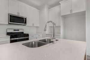 Kitchen with white cabinets, light stone counters, and stainless steel appliances