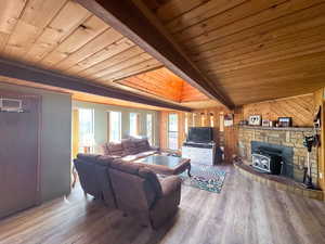 Living room with wooden walls, hardwood / wood-style flooring, a wood stove, and wooden ceiling