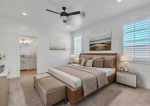 Bedroom with light carpet, ceiling fan, multiple windows, and ensuite bath