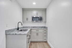 Kitchen with sink, light hardwood / wood-style floors, and light stone counters