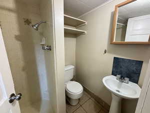 Bathroom featuring tile patterned flooring, tiled shower, toilet, and crown molding