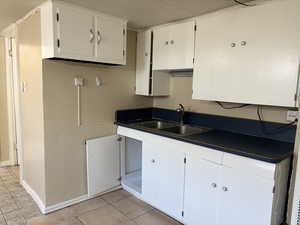 Kitchen with white cabinetry, sink, light tile patterned floors, and ornamental molding