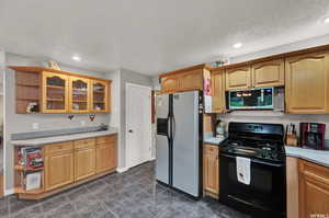 Kitchen featuring dark tile flooring, a textured ceiling, and appliances with stainless steel finishes