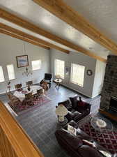 Tiled living room with brick wall, a fireplace, a textured ceiling, and beam ceiling