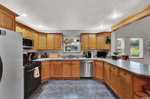 Kitchen with kitchen peninsula, stainless steel appliances, a textured ceiling, sink, and dark tile floors