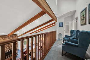 Hallway with lofted ceiling with beams, carpet floors, and a textured ceiling