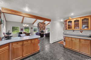 Kitchen with dark tile floors, a baseboard heating unit, a stone fireplace, lofted ceiling with beams, and a textured ceiling