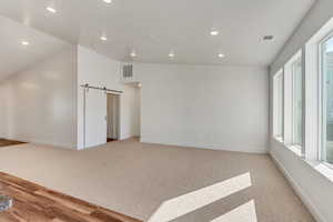 Spare room featuring light hardwood / wood-style floors, lofted ceiling, plenty of natural light, and a barn door