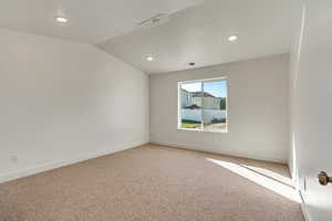 Spare room featuring carpet floors and vaulted ceiling