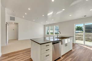 Kitchen with a kitchen island with sink, stainless steel dishwasher, white cabinetry, and plenty of natural light