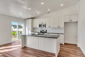 Kitchen with white cabinets, an island with sink, lofted ceiling, appliances with stainless steel finishes, and light hardwood / wood-style floors