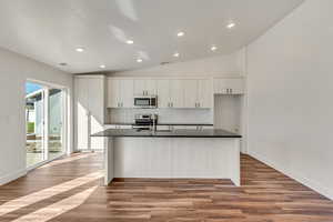 Kitchen featuring light hardwood / wood-style flooring, a kitchen island with sink, white cabinetry, stainless steel appliances, and vaulted ceiling