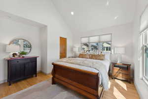 Bedroom with light hardwood / wood-style flooring, high vaulted ceiling, and multiple windows