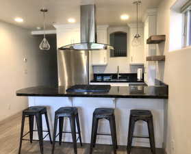 Kitchen with fume extractor, white cabinets, hardwood / wood-style flooring, and pendant lighting