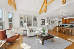 Living room with high vaulted ceiling, light hardwood / wood-style flooring, beam ceiling, and a notable chandelier