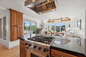 Kitchen featuring dark stone countertops, a chandelier, range hood, stainless steel stove, and light hardwood / wood-style floors