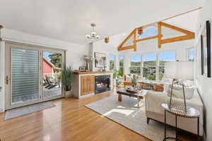 Living room with light wood-type flooring, a wealth of natural light, a chandelier, and vaulted ceiling with beams