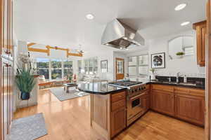 Kitchen with island exhaust hood, kitchen peninsula, premium stove, sink, and light wood-type flooring