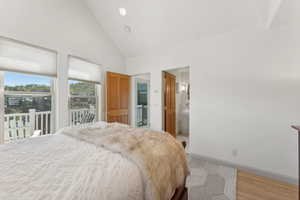 Bedroom with access to exterior, high vaulted ceiling, ensuite bathroom, and light hardwood / wood-style floors