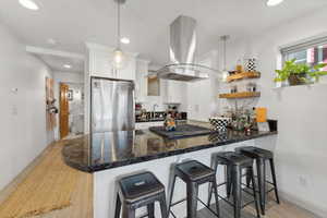 Kitchen with decorative light fixtures, a breakfast bar area, stainless steel appliances, and island range hood