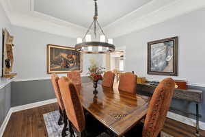 Dining room with a raised ceiling, a chandelier, dark hardwood / wood-style floors, and ornamental molding