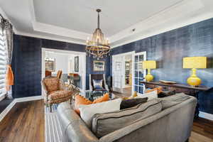 Living room with a notable chandelier, a tray ceiling, hardwood / wood-style floors, ornamental molding, and french doors