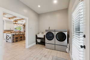 Clothes washing area with washer and dryer, sink, and light wood-type flooring