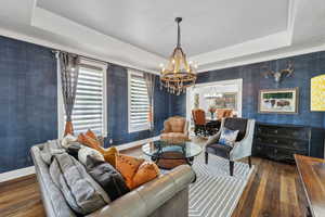 Living room featuring a notable chandelier, a raised ceiling, dark hardwood / wood-style flooring, and ornamental molding