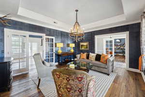 Living room featuring hardwood / wood-style flooring, an inviting chandelier, french doors, and a raised ceiling