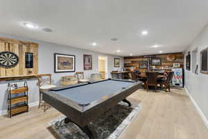 Recreation room featuring bar, wood walls, billiards, and light hardwood / wood-style flooring