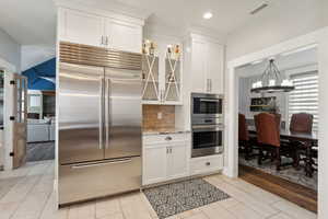 Kitchen featuring stainless steel appliances, tasteful backsplash, white cabinetry, light stone countertops, and light wood-type flooring