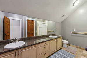 Bathroom featuring a textured ceiling, toilet, and dual bowl vanity