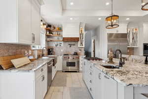 Kitchen featuring tasteful backsplash, premium appliances, white cabinets, sink, and light tile floors