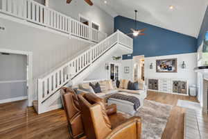 Living room with high vaulted ceiling, ceiling fan, and hardwood / wood-style flooring