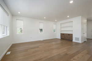 Unfurnished living room with built in features and hardwood / wood-style floors