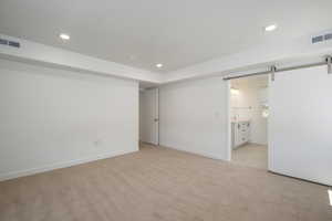 Unfurnished bedroom featuring a barn door, light colored carpet, and ensuite bathroom